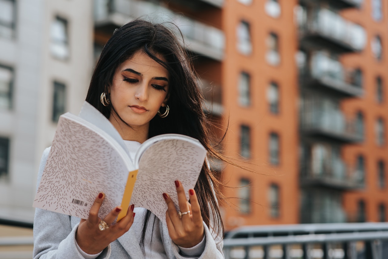 Focused ethnic woman reading magazine in city